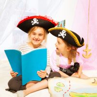Two happy girls in pirate's costumes, reading blanked book about pirate's treasures
