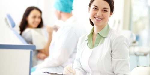 Pretty nurse looking at camera with smile on background of dentist and patient